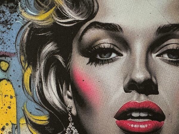 A close-up of a detailed DTF-printed design featuring a stylized portrait of a woman with bold red lips, dramatic eye makeup, and golden highlights in her hair. The artwork has a realistic, high-contrast look with graffiti-style elements in the background, showcasing the vibrant colors and fine detail achievable with DTF printing. direct to film