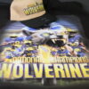 A DTF-printed t-shirt featuring a Wolverines National Champions design with a fierce, growling wolverine, a group of football players in blue and yellow uniforms, and a championship trophy. The bold yellow and blue text pops against the dark background, showcasing the sharp details and vibrant colors of DTF printing. A matching beige and black cap with the same Wolverines National Champions design is placed on top.